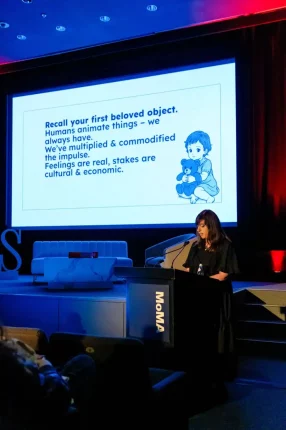 Katherine Dee, Sprecherin auf dem Visions Summit auf der Bühne. Hinter ihr ein Screen mit den Worten (übersetzt auf Deutsch) "Erinnere dich an dein erstes geliebtes Objekt. Menschen beleben Dinge - schon immer. Wir haben den Impuls vermehrt und kommerzialisiert. Gefühle sind real, Einsätze sind Kultur & Wirtschaft."